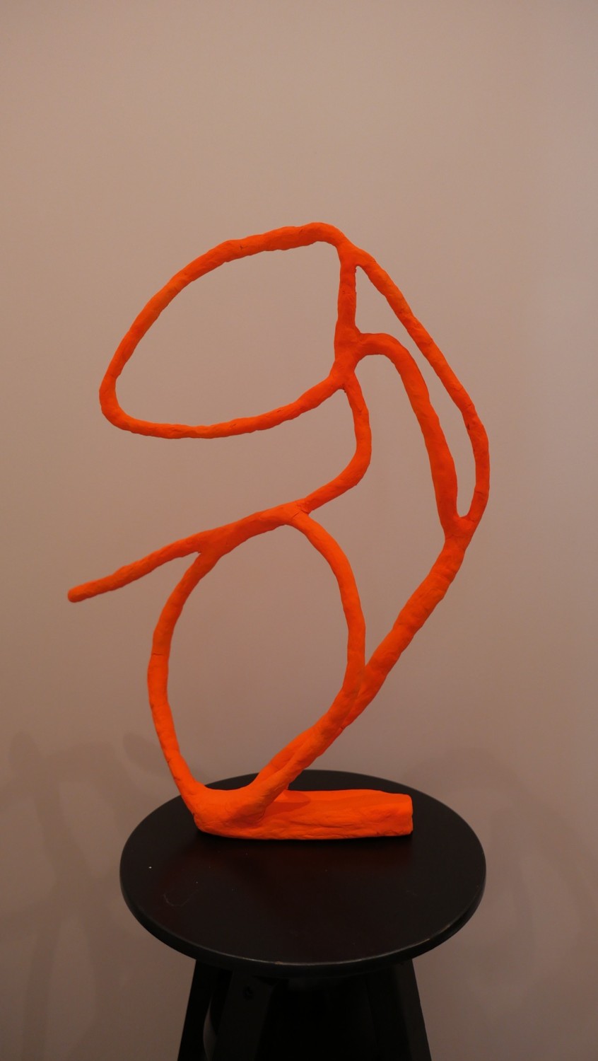 Orange open-form sculpture on a black pedestal